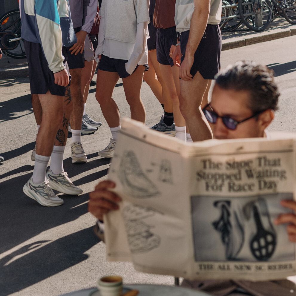 A man reading a newspaper with runners wearing New Balance sneakers in the background. New Balance running sneakers placed on a newspaper.